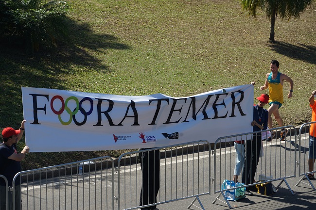 За дистанції марафону стоять глядачі, які протестують проти кривавого бразильського режиму, що використовує Олімпіаду в своїх брудних політичних цілях